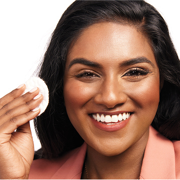Model smiling at the camera preparing to take off eye makeup with a pad